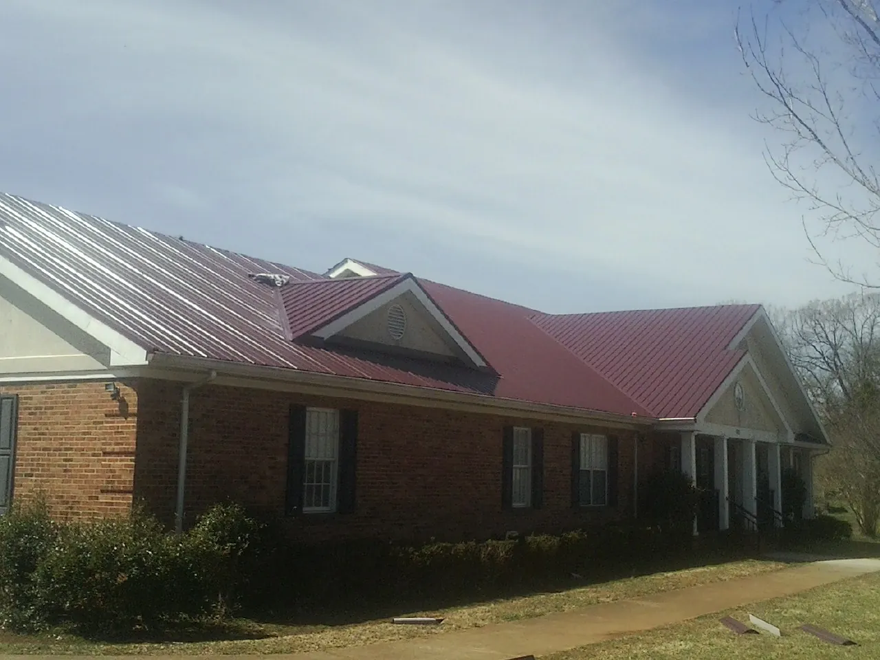 Red metal roof with gabled entries on a long brick building, from a Hail Damage Roof Repair job in Lamont